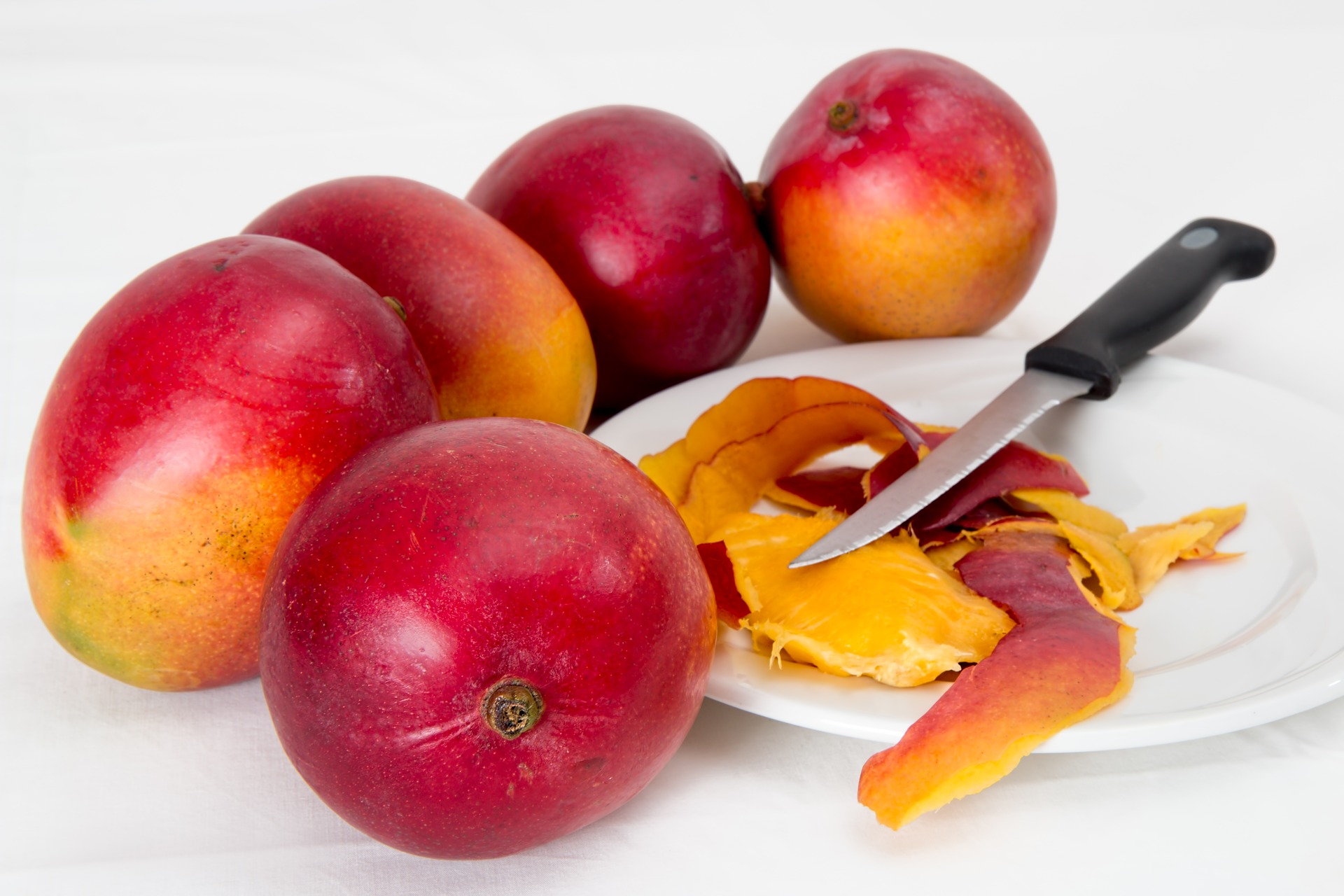 5 mango fruits around white plate with knife and mango peels