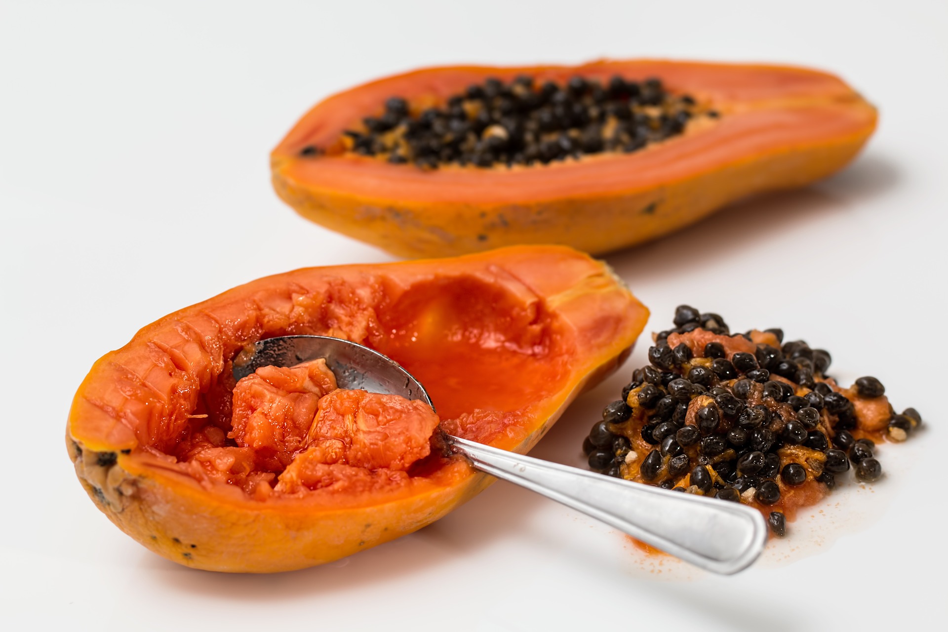 Papaya fruit sliced in half with spoon scooping out seeds